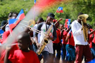 photo of people playing instruments while others wave the flag of Haiti