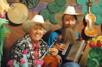photo of Jeanie McLerie holding a fiddle and Ken Keppeler holding an accordion both wearing cowboy hats