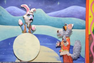 photo of puppet of a rabbit on the moon and a grey coyote looking up at the rabbit