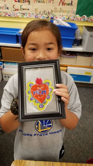 photo of child holding up a repujado of a heart that says "mom" on the bottom