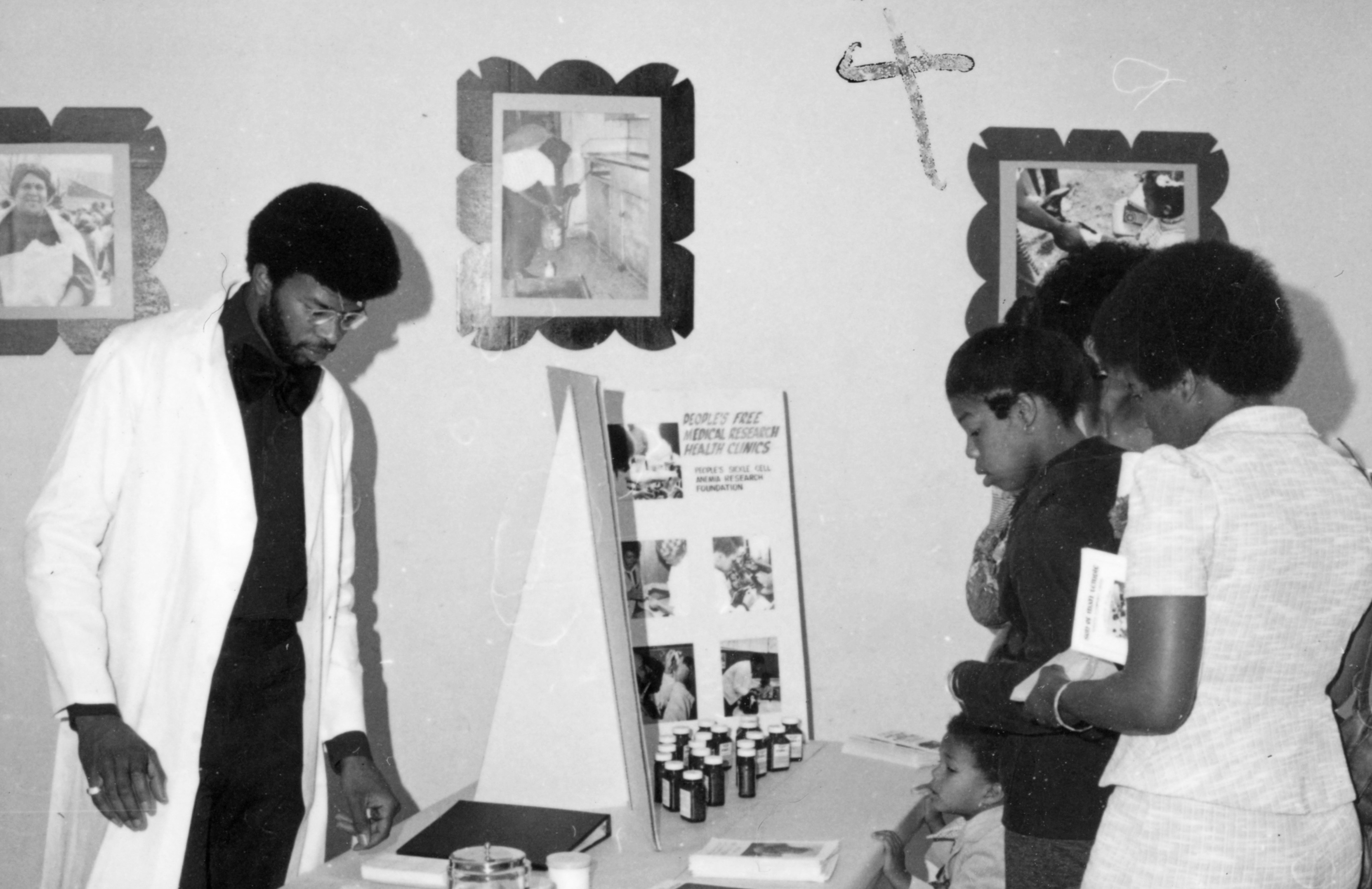 Black and white photograph of a doctor explaining a medical procedure or material to a few onlookers or patients
