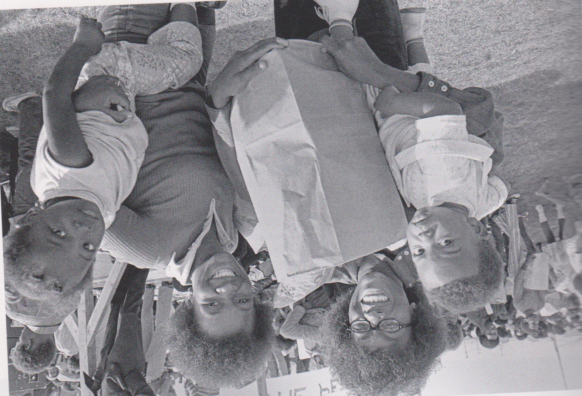 Black and white photograph of a Black mother and three children holding grocery bags and smiling at the camera