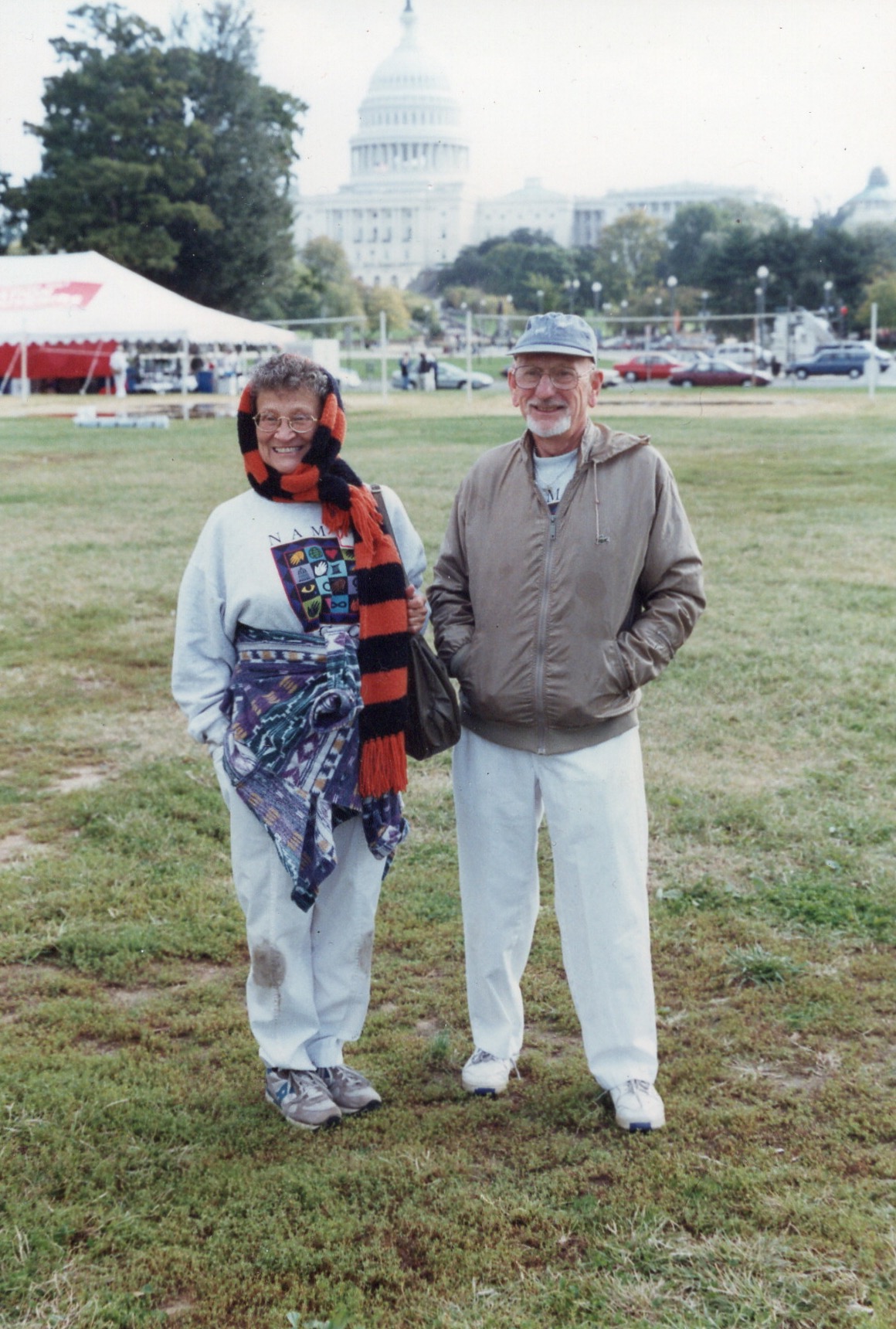 An older man and woman in a field smiling at a camera. In the distance, the United States capital is visible