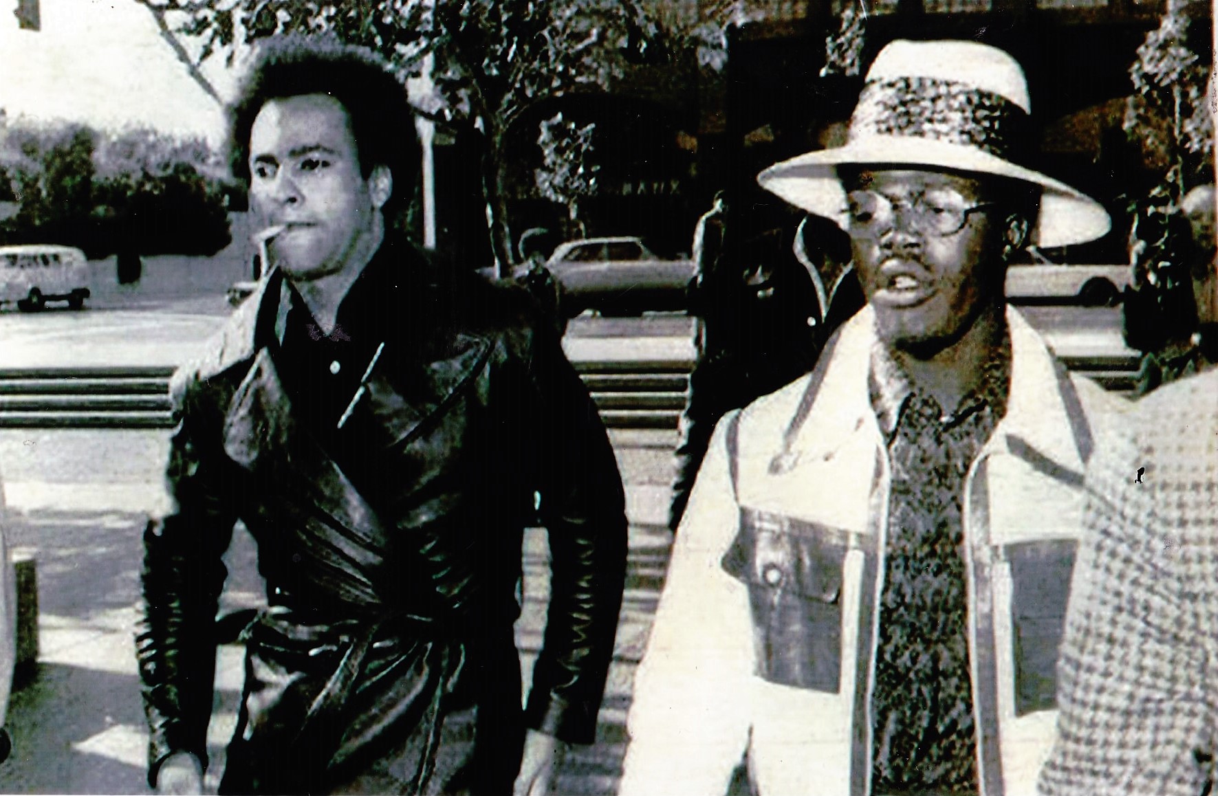 A photograph of two men dressed sharply walking across a street with purpose