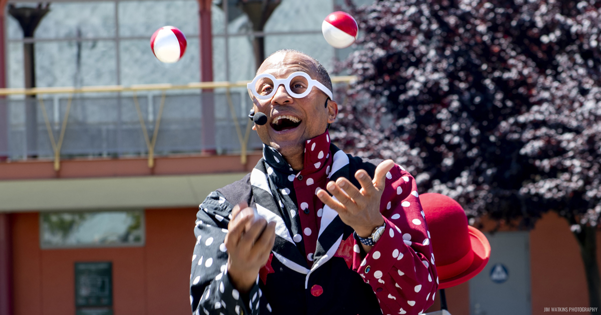 photo of Unique Derique wearing large white glasses and juggling red and white balls outside 