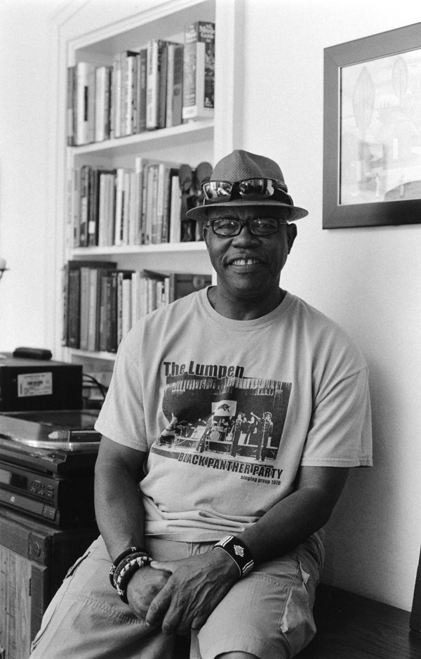 Man smiling at a camera, wearing a top hat with a bookshelf behind him