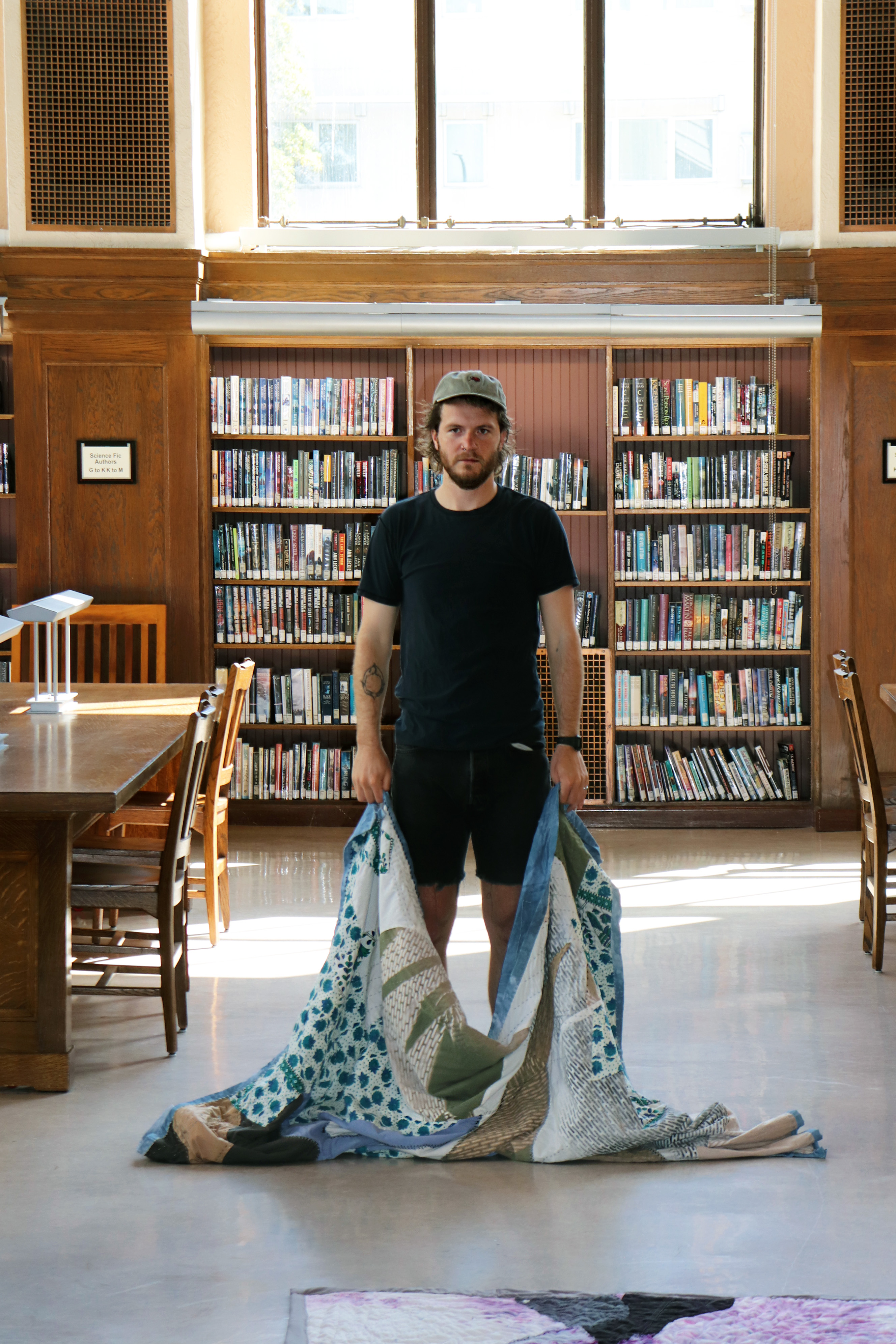 Artist Cordy Joan holding a quilt draped onto the floor of the Berkeley Public Library