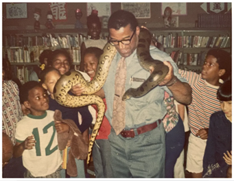 Jim Jacobs with snake around shoulders and children looking on