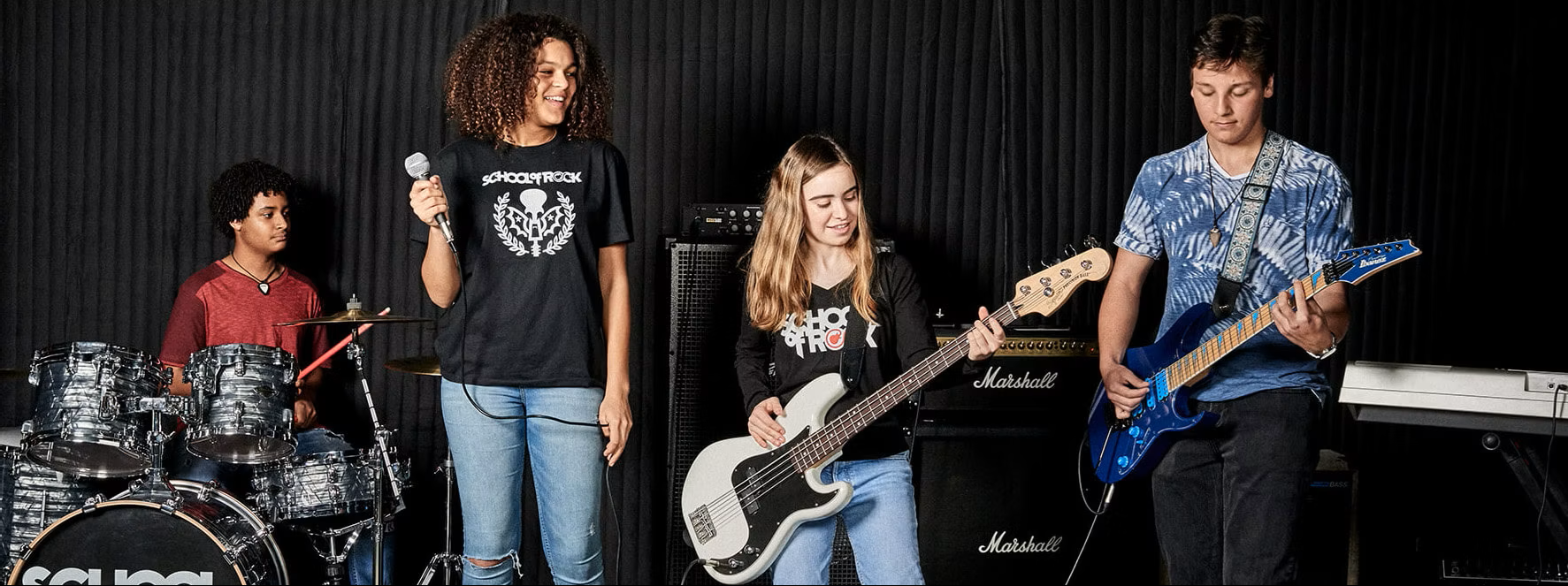Teen children playing rock instruments guitar, bass, drums, microphone