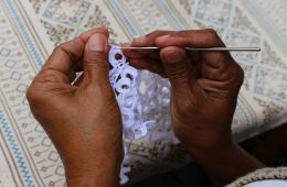 Black hands holding a small crochet hook, making a doilie