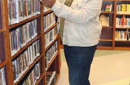 man in front of book shelf looking at books wearing a mask