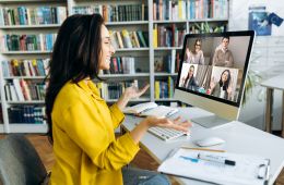 Woman in yellow talking on Zoom call with 4 other people on the computer screen.