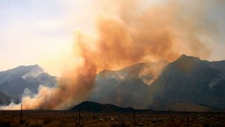 photo of orange smoke in front of gray mountains with a wire fence in front