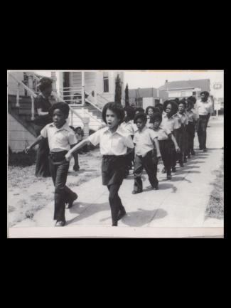 Children in white and black uniforms marching down the sidewalk