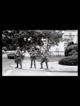 Three national guardsmen in gear reading the Black Panther newspaper on the sidewalk