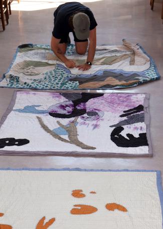 Curator Cordy Joan kneeling and working on several quilts on the ground