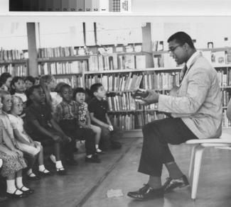 Librarian Jim Jacobs plays guitar while children watch and listen