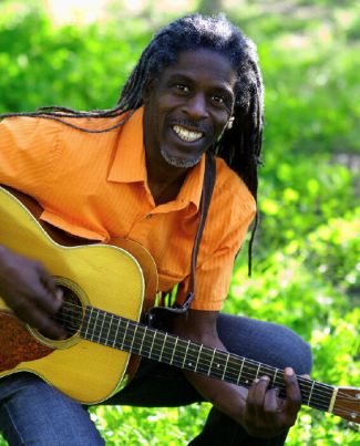 photo of Asheba sitting down playing guitar outside