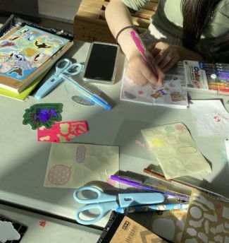 photo of table top with zine supplies strewn about and someone working on a zine!