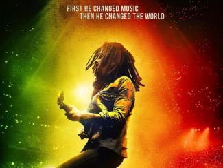 Bob Marley: One Love movie image featuring the world famous musician playing the guitar against a red, green, and gold background