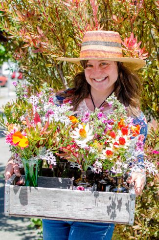 Woman with straw hat holding a box of multicolored flowers.