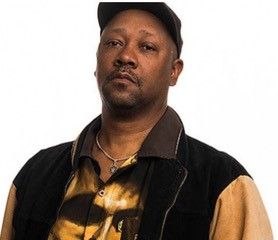 Headshot of Davey D, African American male wearing a black ball cap and a black and  gold shirt