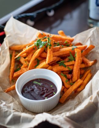 A bowl of sweet potato fries with a cup of dipping sauce