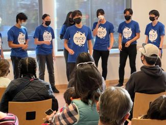 7 singers wearing masks and blue t-shirts that say "NiCE" 