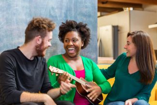 African American Woman playing Ukulele and laughing with a White man and White woman.
