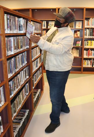 man in front of book shelf looking at books wearing a mask