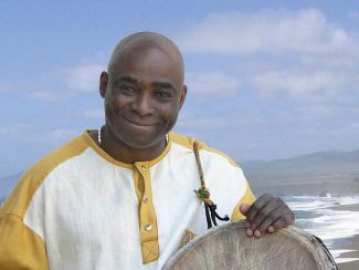 photo of musician Onye Onyemaechi holding a drum in front of a blue sky