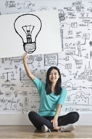 woman sitting with raised hand holding a drawing of a lightbulb