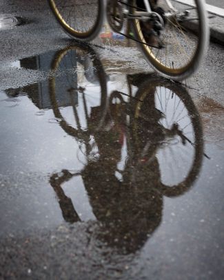 Bike and rider reflected in a puddle of water.
