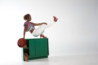photo of dancer Quynn Johnson on top of green locker balancing on one bent leg, kicking out the other leg in front of her