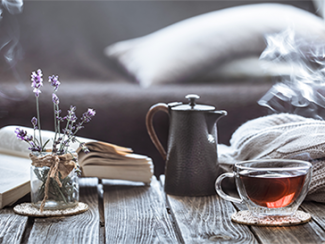 Cup of tea, lavender in a jar, open book and a sweater on a coffee table