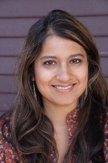 Headshot of Sonali Kolhatkar, a woman of Indian descent with long hair and a red shirt.