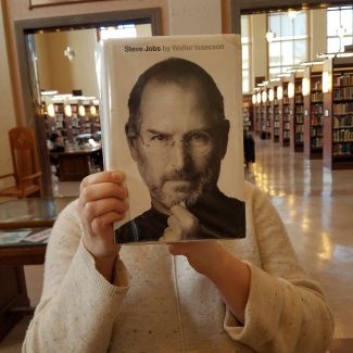 Person holding a book with the face of Steve Jobs as the cover