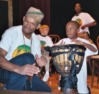 photo of Mr. King instructing a young boy how to play a djembe drum 