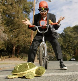 photo of Unique Derique on a bike wearing a helmet with his hands outstretched in frustration while waiting for a turtle to cross the road.