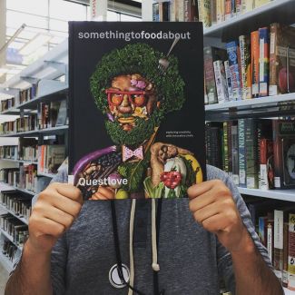 Person holding a book of a face made of food in front of their face.