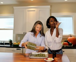 Two women in a kitchen examining a bowl of cannabis