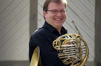 Man smiling while holding a French horn.