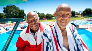 Two older americans smiling on the deck of a lap pool.
