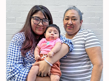 Two people presenting as female posing and holding a baby