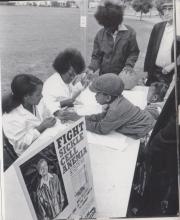 Black and white photograph of children being seen by nurses at a table in a public park during a community event