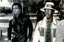 A photograph of two men dressed sharply walking across a street with purpose