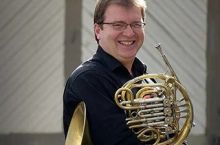 Man smiling while holding a French horn.