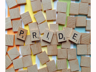 "Pride" in scrabble tiles over a rainbow. 